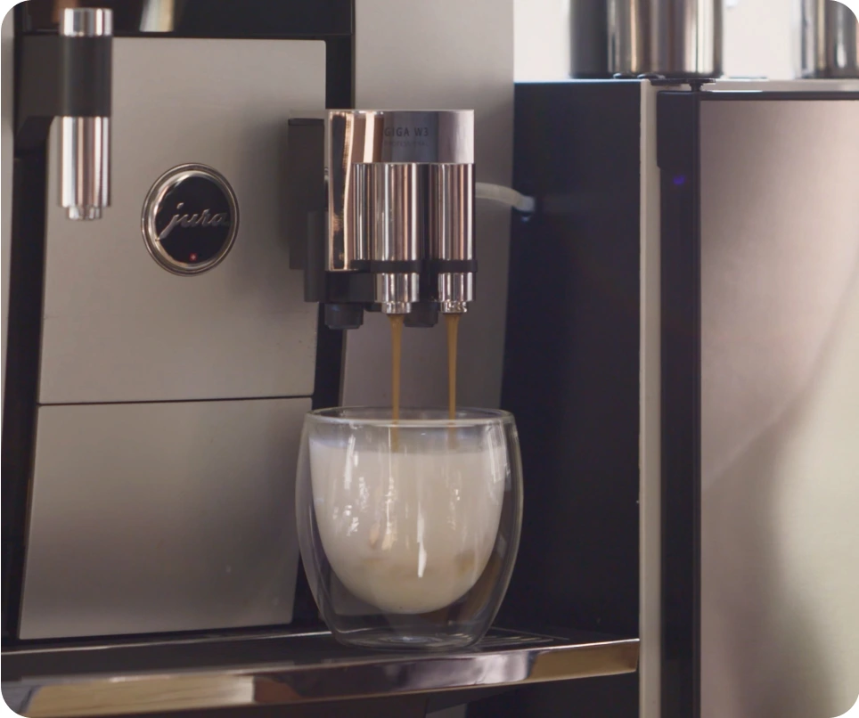 Coffee cup filling with espresso and steamed milk beneath a modern office coffee machine.